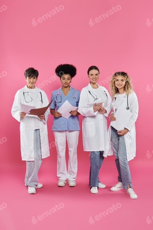 Preview: smiling interracial doctors holding paper folders and digital tablet on pink, breast cancer month