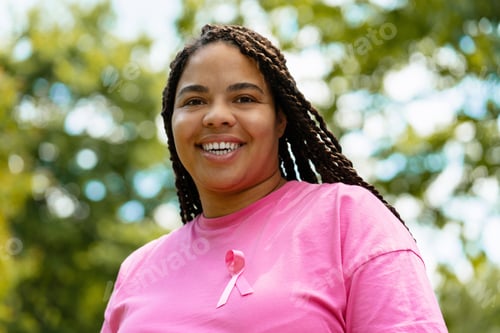 Preview: Young woman wearing pink ribbon smiling in a park during breast cancer awareness month