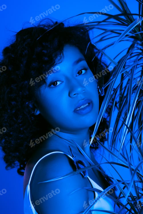 Preview: curly african american woman with butterflies on body looking at camera near palm leaves isolated on