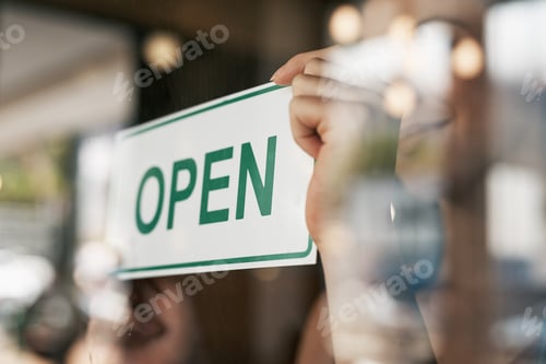 Preview: Cropped shot of a woman hanging an open sign on the door of her store