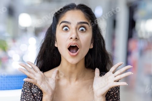 Preview: Excited young indian woman with surprised expression in shopping mall
