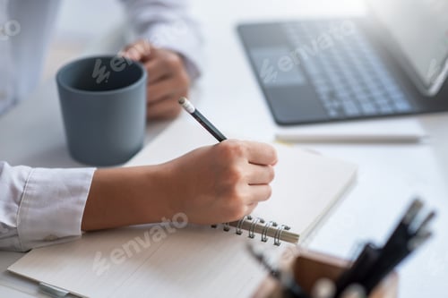 Preview: Business woman using a pencil to taking notes in his notebook. Along with your favorite coffee at th