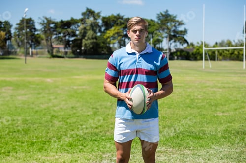 Preview: Holding rugby ball, athlete wearing striped jersey on field, looking determined, copy space