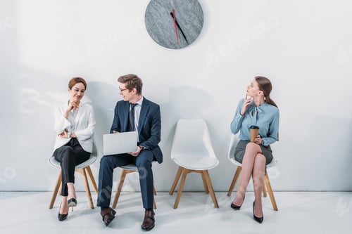 Preview: woman with paper cup looking at clock near employees sitting on chairs