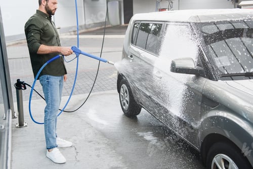 Preview: handsome man cleaning car at car wash with high pressure water jet