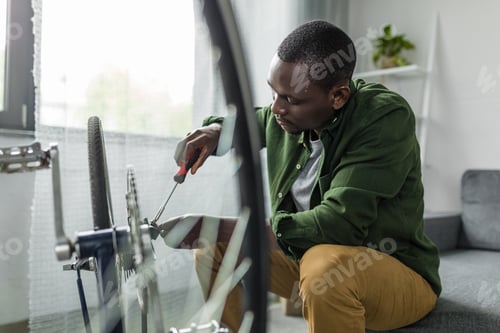 Preview: concentrated afro man repairing bicycle with screwdriver at home
