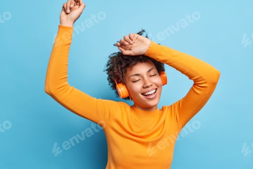Preview: Photo of relaxed curly haired young woman keeps eyes closed dances and catches every bit of music sm