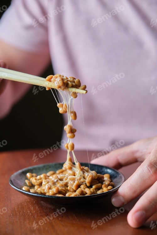 Preview: Unrecognizable man eating natto fermented soy beans with chopsticks.