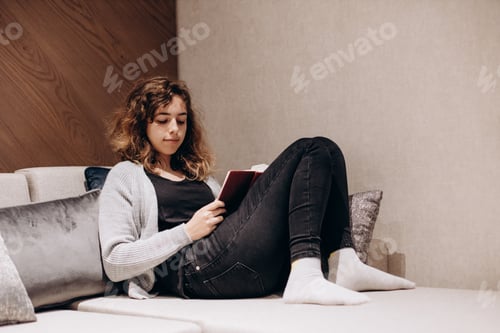 Preview: Teenager girl reading book on the couch at home