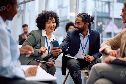 Preview: Happy black colleagues using cell phone during business seminar in board room.