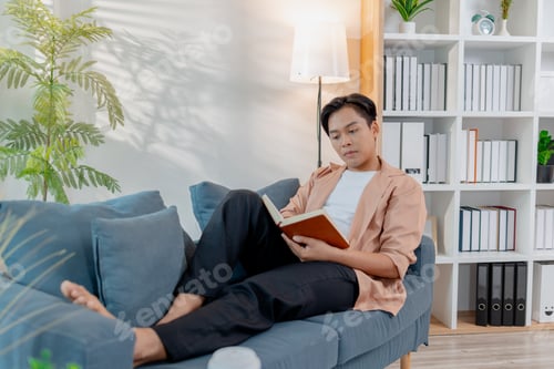 Preview: A young man sits comfortably on a sofa reading a book, appearing thoughtful and focused.