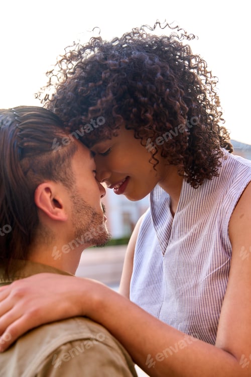 Preview: Young couple sharing intimate moment, touching foreheads outdoors