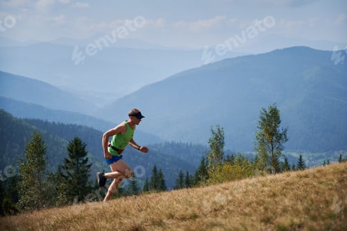 Preview: Athletic young man running up the hill in mountains.