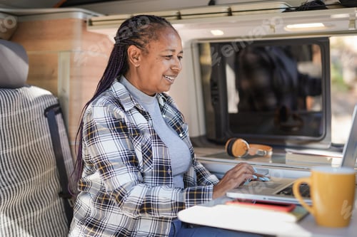 Preview: African senior woman working inside mini van camper with computer laptop - Digital nomand concept