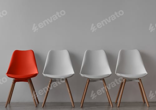 Preview: Three vacant white chairs and one red on gray wall background in office or room