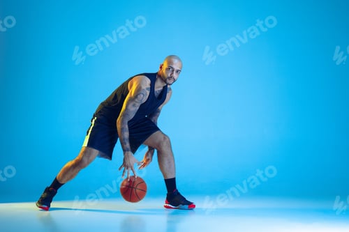 Preview: Young basketball player training isolated on blue studio background in neon light