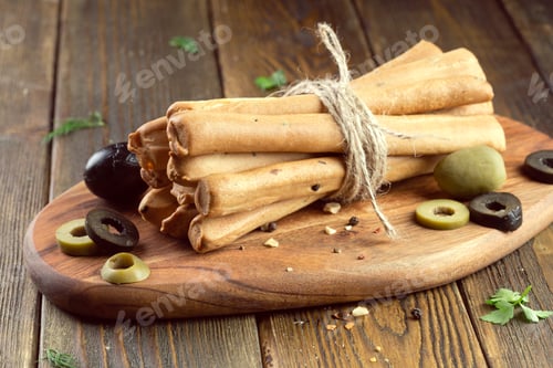 Preview: Artisan breadsticks with olives on a rustic wooden board in a cozy kitchen setting
