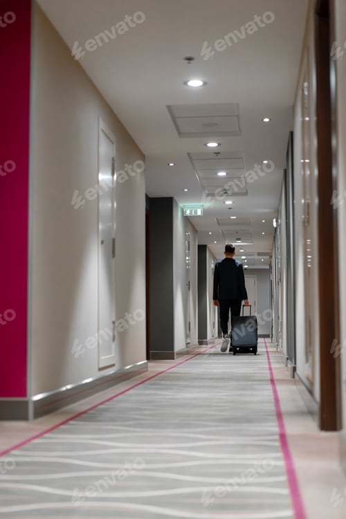 Preview: A man with a suitcase walks down the hotel corridor a back view of a businessman on trip