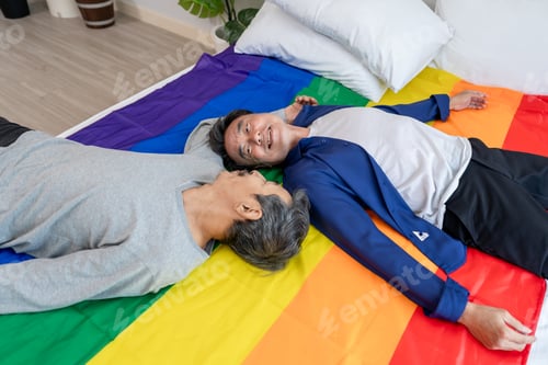 Preview: Asian senior elderly male gay couple lying down on bed with rainbow flag.
