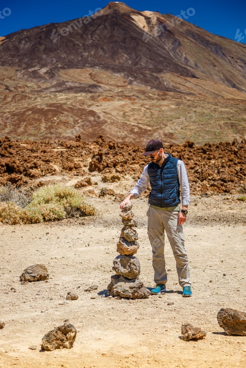 Preview: A tourist man building a cairn for balance or adventure concept, Teide in the background, Tenerife
