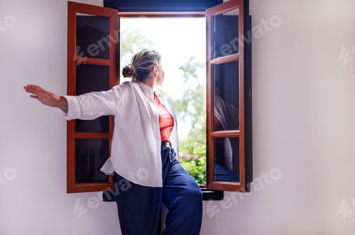 Preview: Woman with light hair, wearing a white shirt and blue pants, is leaning out of a window