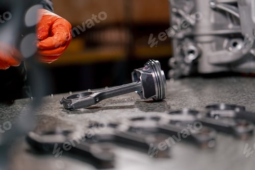 Preview: close-up At a service station on the table young engine repairman assembles a new piston part