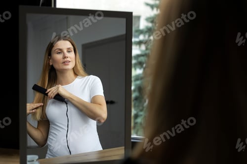 Preview: Beautiful pregnant woman using hair straightener looking at the mirror. Hairstyle, morning routine