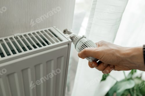 Preview: A man regulates the temperature on the radiator at home. Rising prices for heating in households.