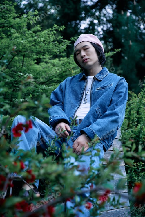 Preview: Stylish young man enjoys a serene moment in a lush green park in denim attire