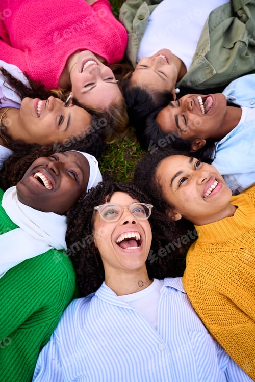 Preview: Multiracial group of young only female community friends having fun lying in circle on grass.