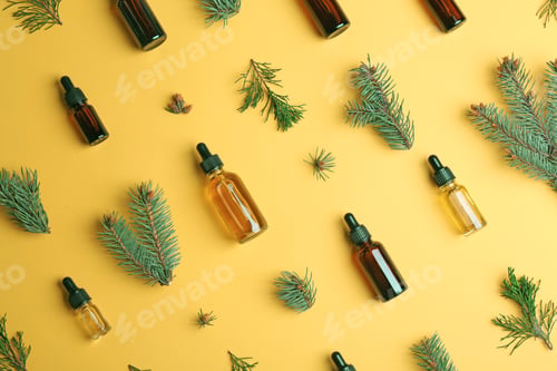 Preview: Little bottles with essential oils among pine branches on color background, flat lay