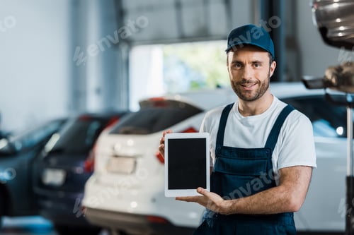 Preview: cheerful car mechanic holding digital tablet with blank screen in car service