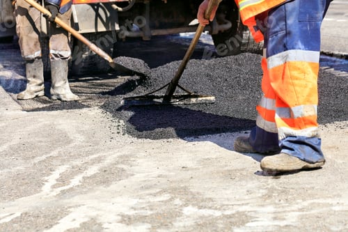 Preview: Road service worker shoveling new asphalt during construction and patching of a road