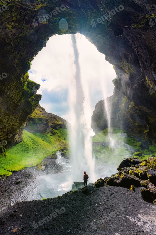 Preview: Powerful waterfall Kvernufoss flowing from cliff with tourist standing in summer at Iceland