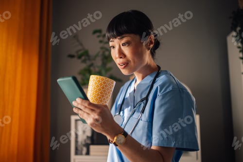 Preview: Asian woman nurse reacting astonished on her mobile phone with a mug