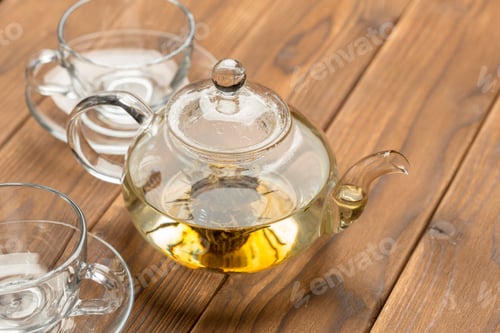Preview: Clear glass teapot and cups on wooden table with brewed tea ready to serve