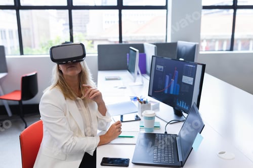 Preview: VR headset resting on office desk with dual monitors showing graphs and coffee cup near window