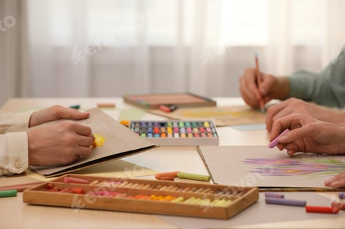 Preview: Artists drawing with soft pastels and pencils at table indoors, closeup