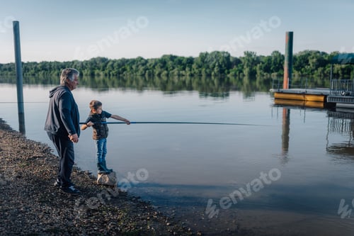 Preview: Grandfather teaching grandson how to fish on riverbank