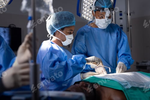 Preview: Diverse female doctors with face masks doing surgery in hospital operating room