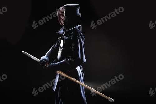 Preview: Side view of kendo fighter in traditional helmet holding bamboo sword on black