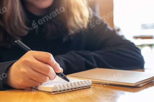 Preview: Closeup image of a woman writing on blank notebook on wooden table