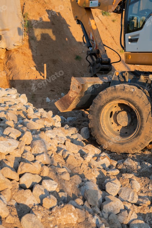 Preview: Excavator works on gravel site at sunset, casting shadows on earthy terrain in warm golden light