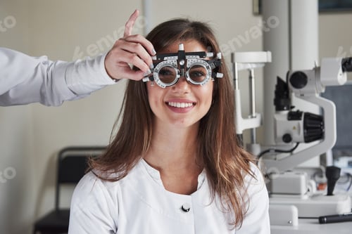 Preview: Girl wears glasses in eye clinic and smiling at background of medical equipment