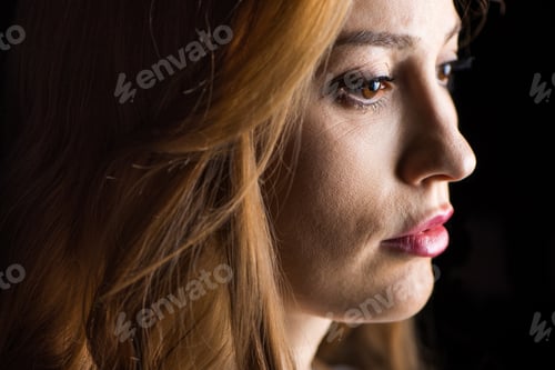 Preview: Close-up side view of serious young woman isolated on black