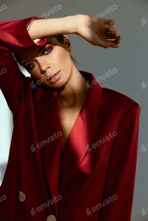 Preview: pretty woman with bright makeup holds her hand above her head shading off the light red jacket