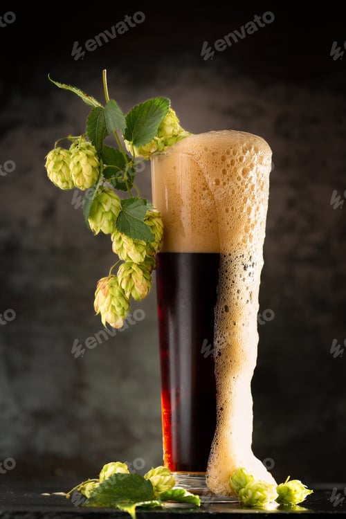 Preview: Glass of dark beer with hops around on a dark background
