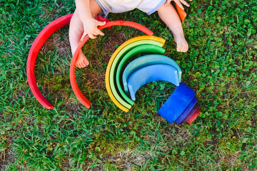 Preview: Baby playing with a colorful wooden rainbow on the grass