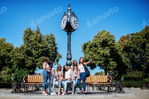 Preview: Six beautiful young girls sitting on a bench next to the old street clock in the park.