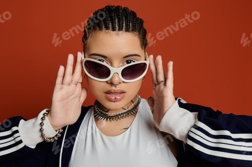 Preview: Stylish young woman with braids and sunglasses expressing confidence against a vibrant background